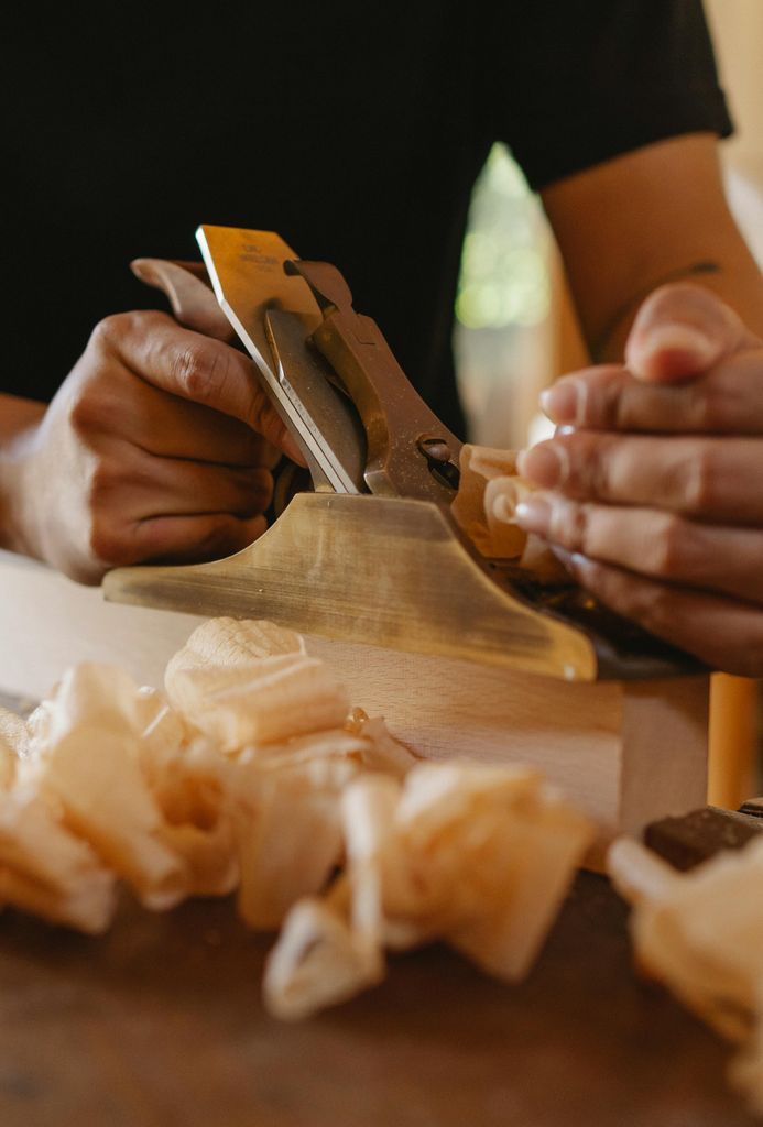 Crop joiner with manual jack plane shaping timber plank at workbench in own studio