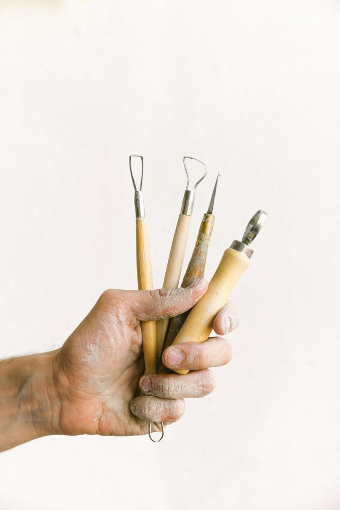 Anonymous male master with set of instrument for clay modeling in dirty hand standing on white background in professional workshop