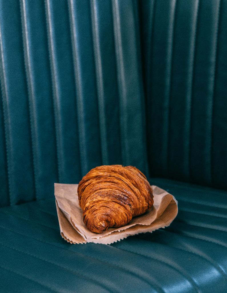 Tasty freshly baked croissant on parchment paper placed on dark leather sofa in daylight